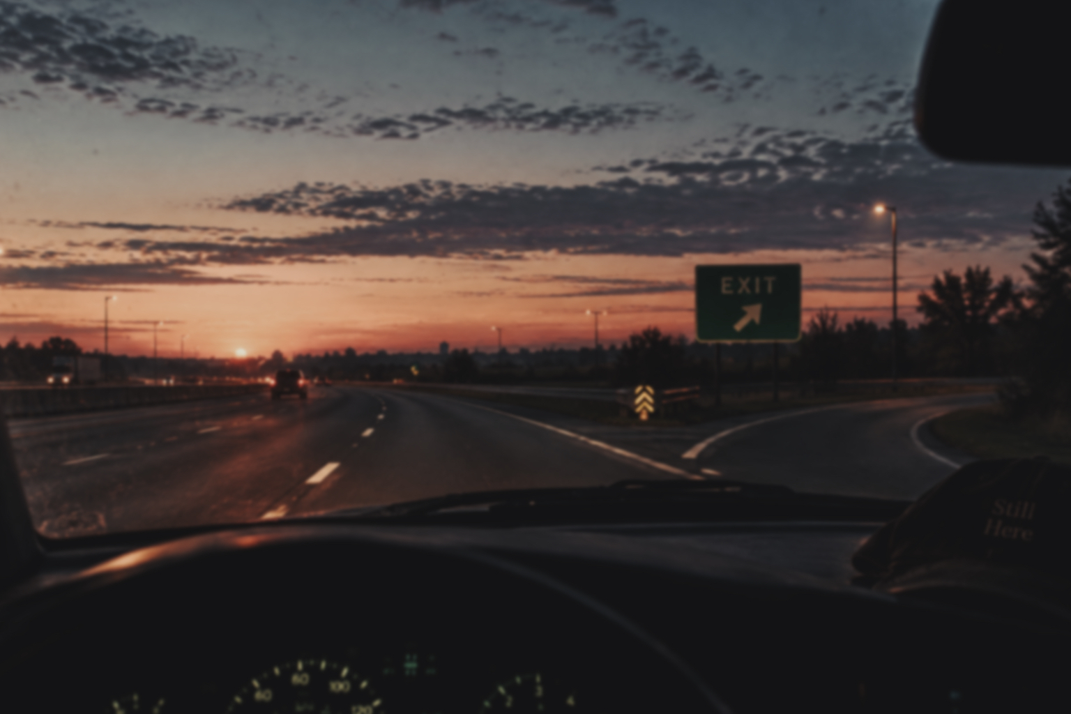 A highway exit seen through a windshield at first light.